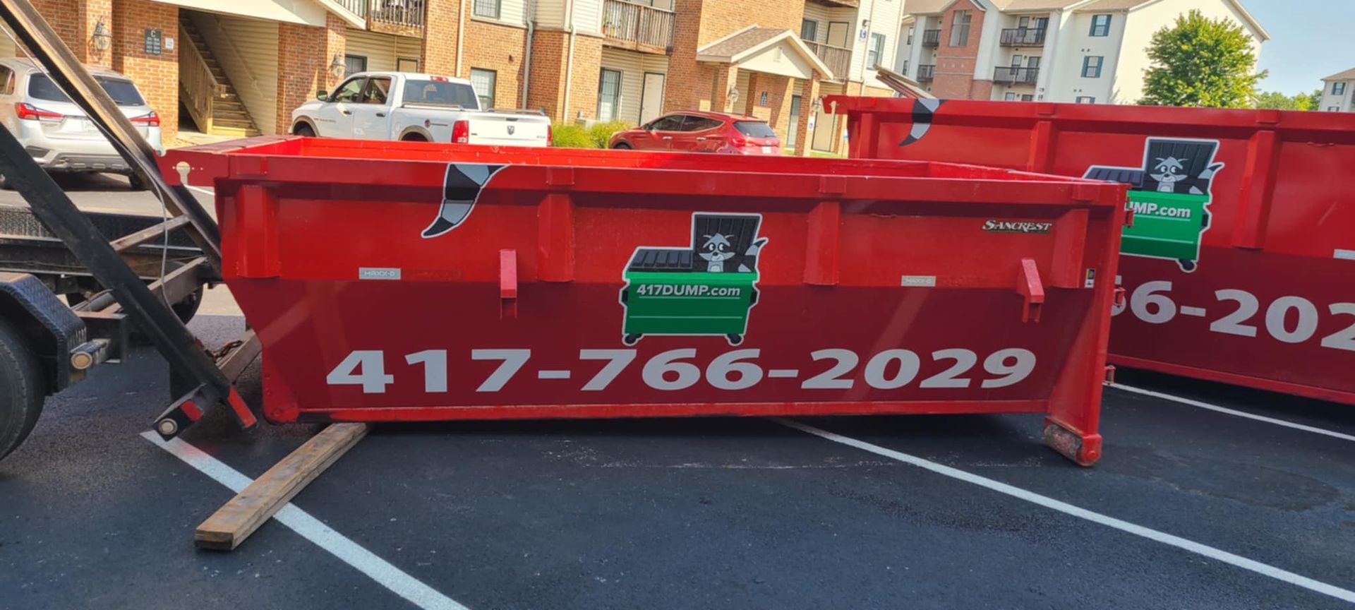 Red dumpster with the phone number 417-766-2029 in a parking lot.