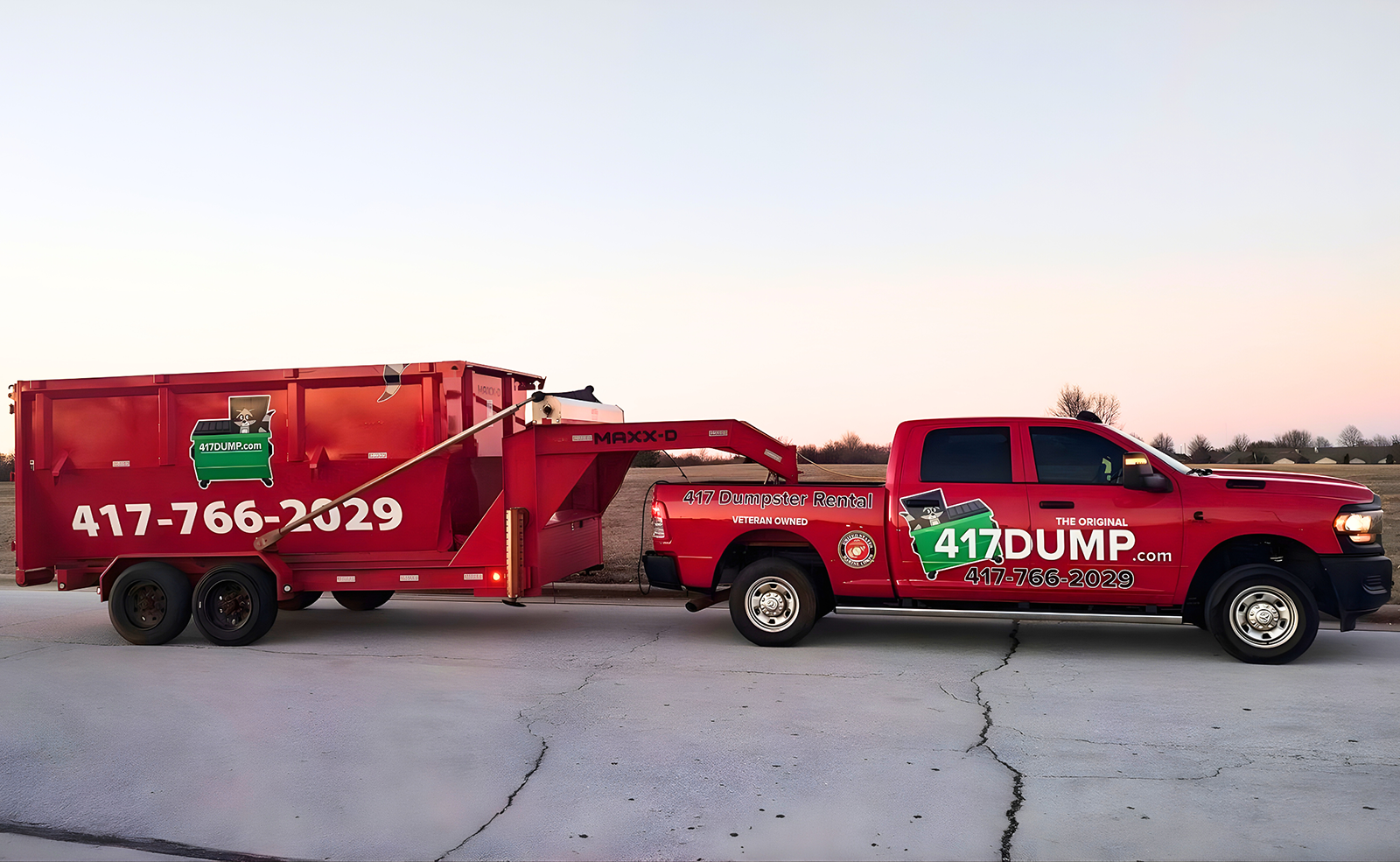 Red pickup truck towing a red dumpster trailer. The truck and trailer have 417 DUMP.in logo and phone number.