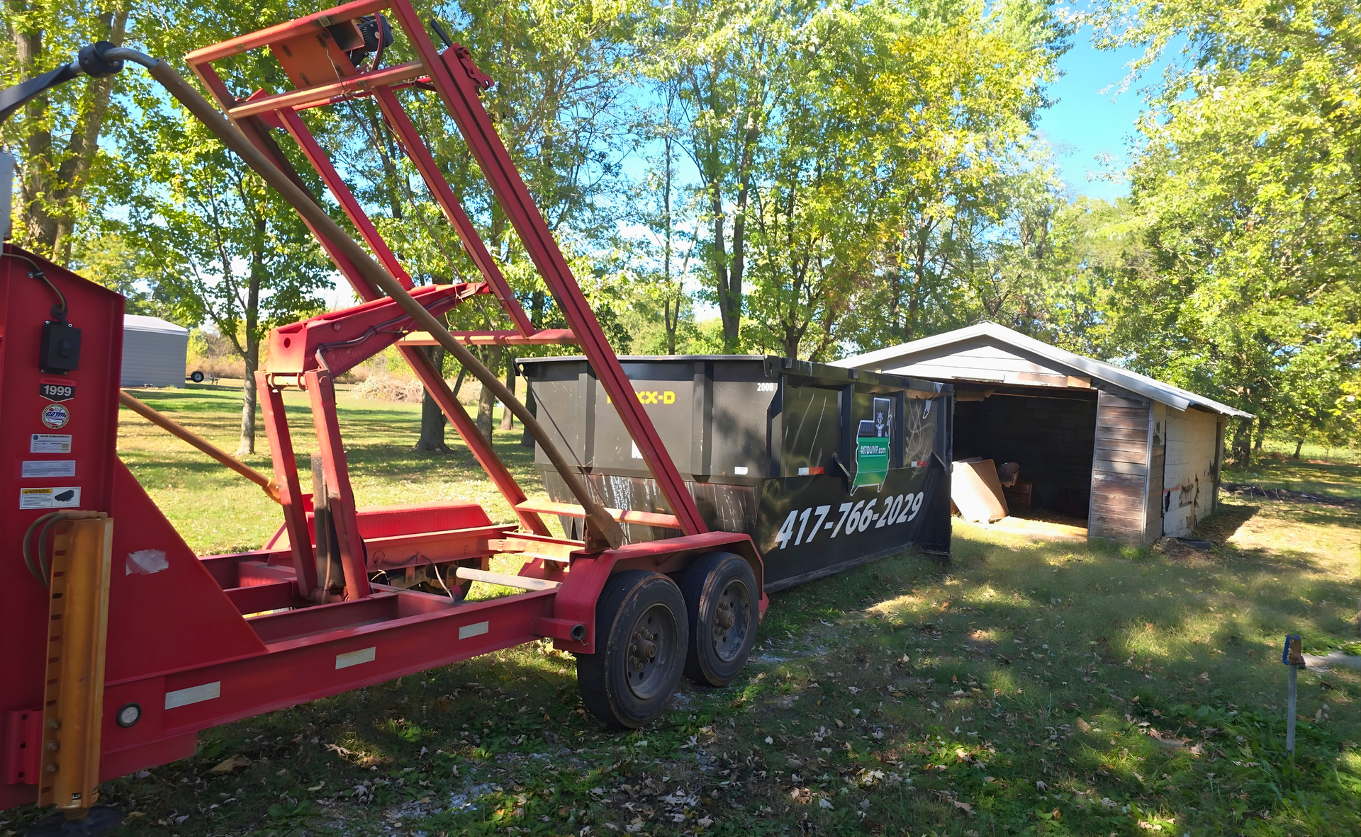 Red trailer with a dumpster beside a weathered shed.