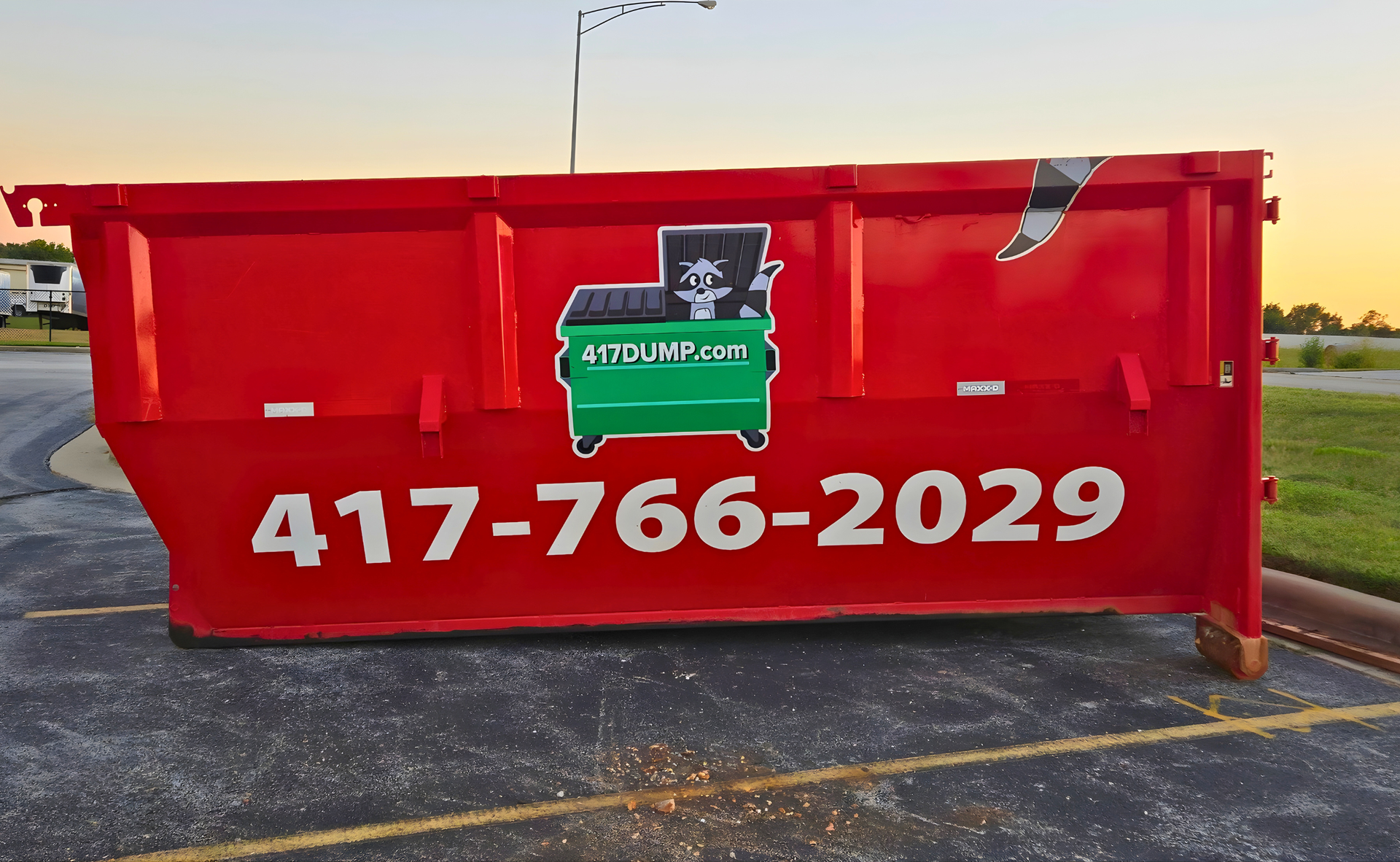 Red dumpster with business logo, phone number, in parking lot.