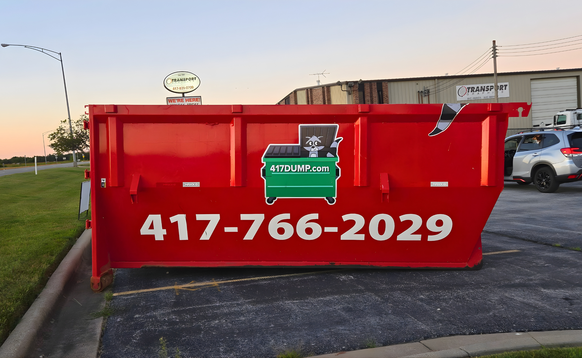 Red dumpster with green logo and phone number, parked outdoors.