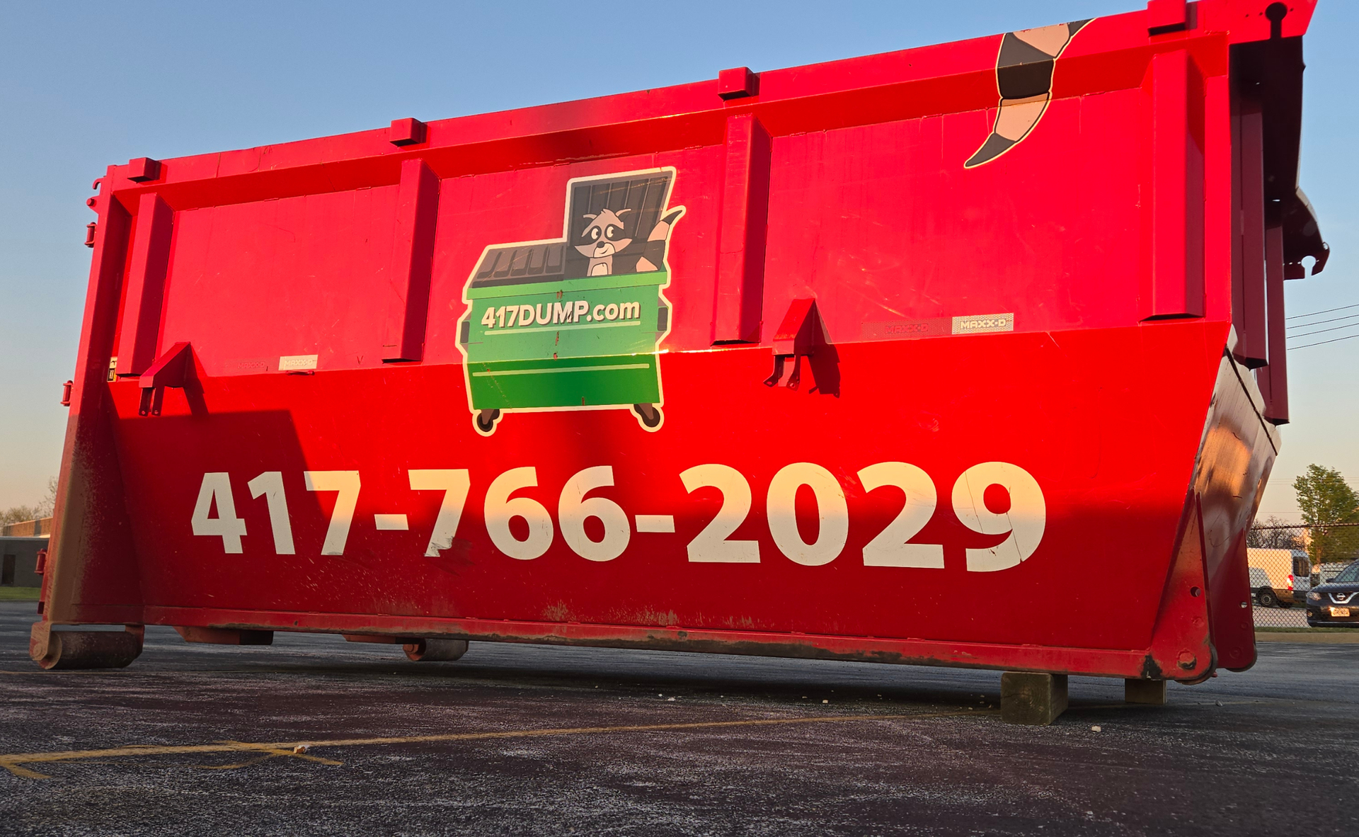 Red dumpster with a green and black logo and phone number 417-766-2029.