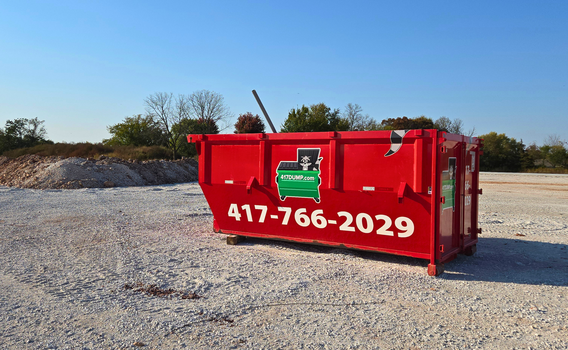 Red dumpster with phone number on gravel lot.