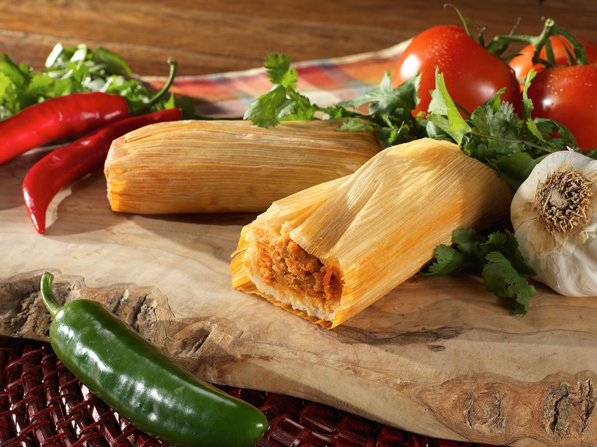 Tamales with red and green peppers on a wooden cutting board