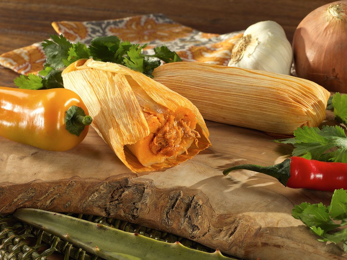Fresh corn, tamales, chili peppers, and herbs on a rustic wooden table