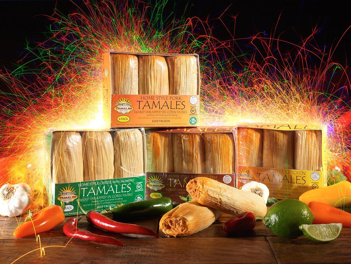 Stacked Tamales boxes with assorted peppers, lime, and garlic on a colorful, glowing background