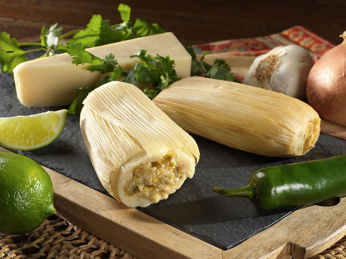 Fresh tamales on a cutting board with lime, chili pepper, cheese, onion, and cilantro