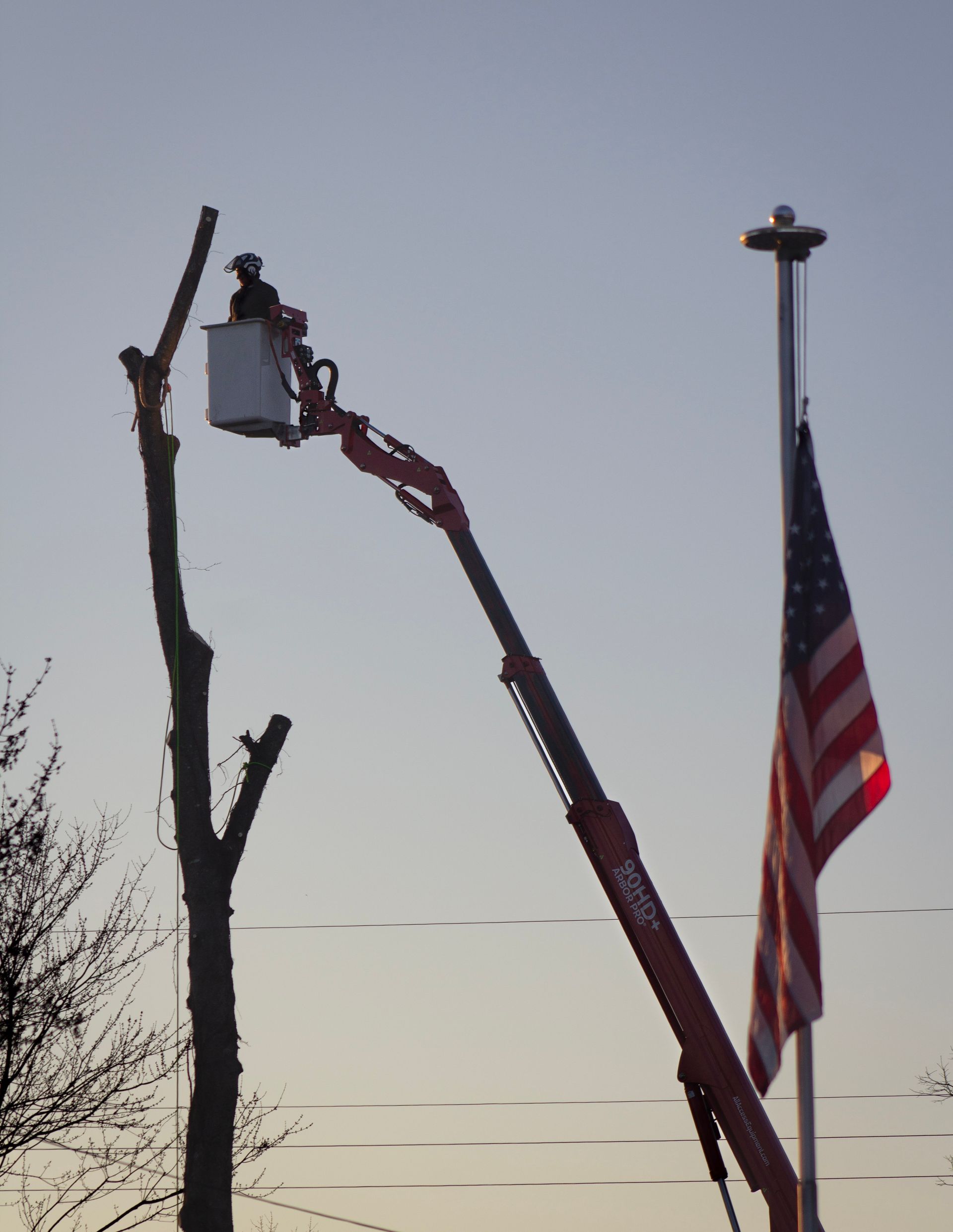 A man in a bucket on a crane next to an american flag