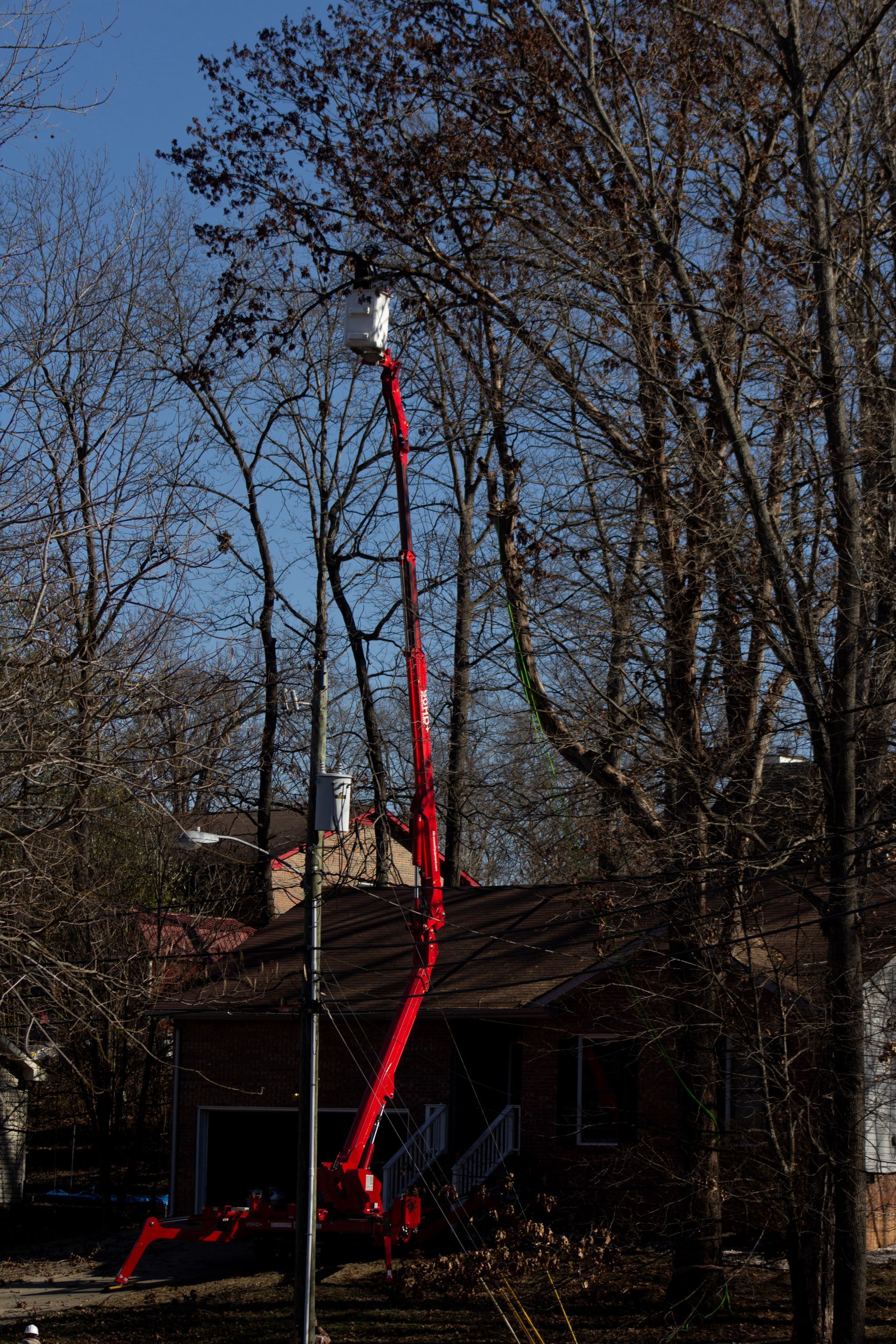 A red crane is cutting a tree in front of a house.
