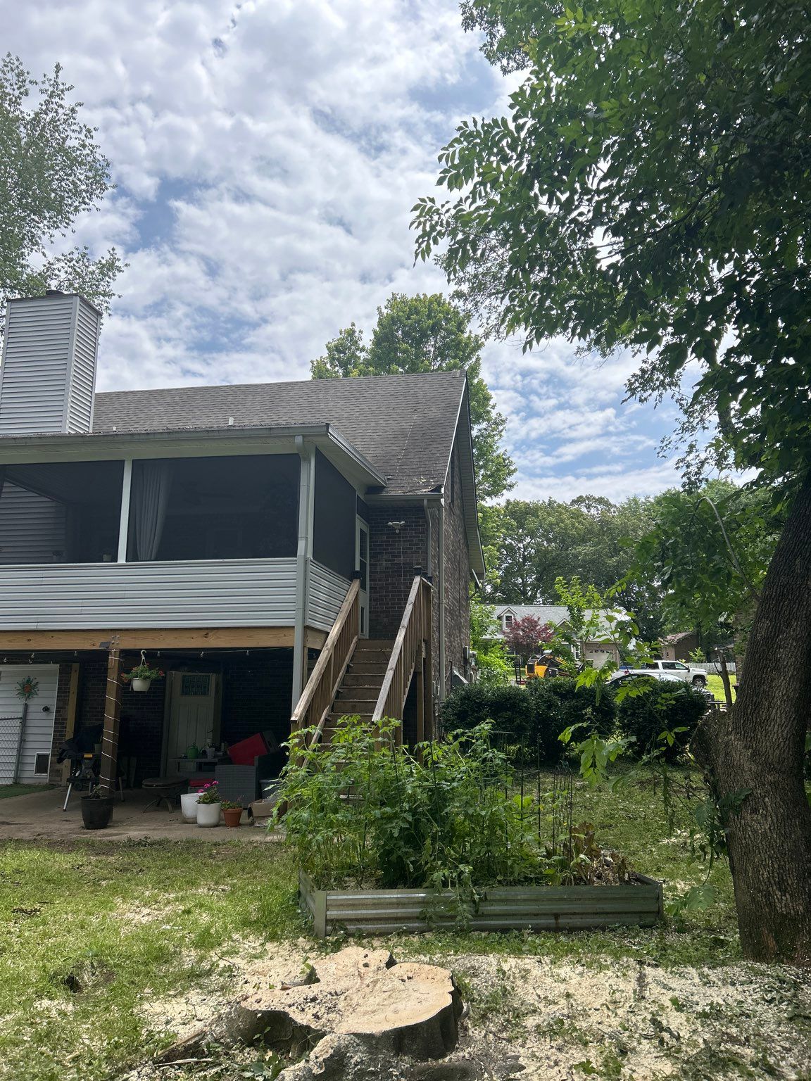 A house with stairs leading up to the second floor and a tree stump in front of it.