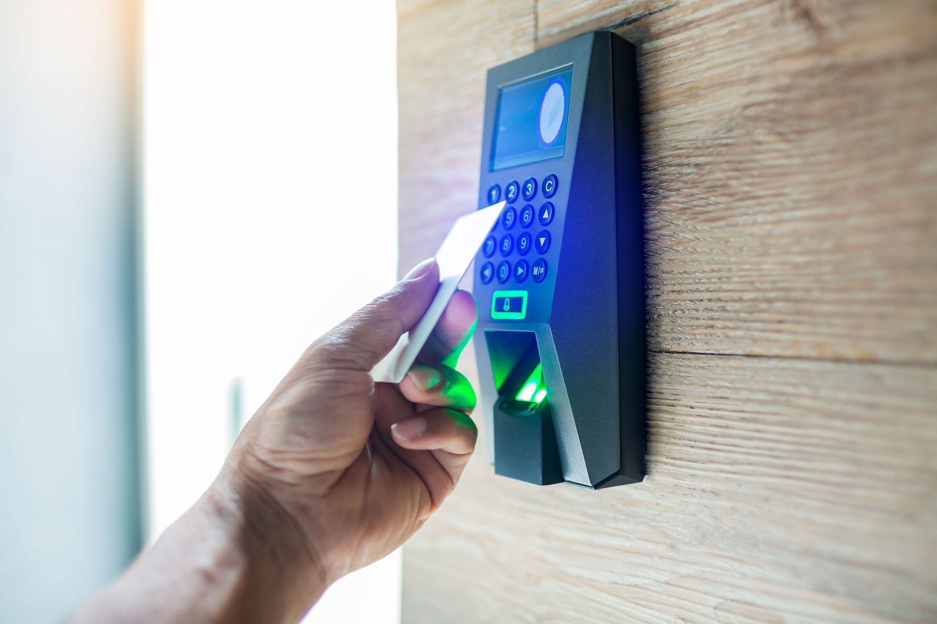 Person scanning an access card on a door security system with a keypad and fingerprint scanner.