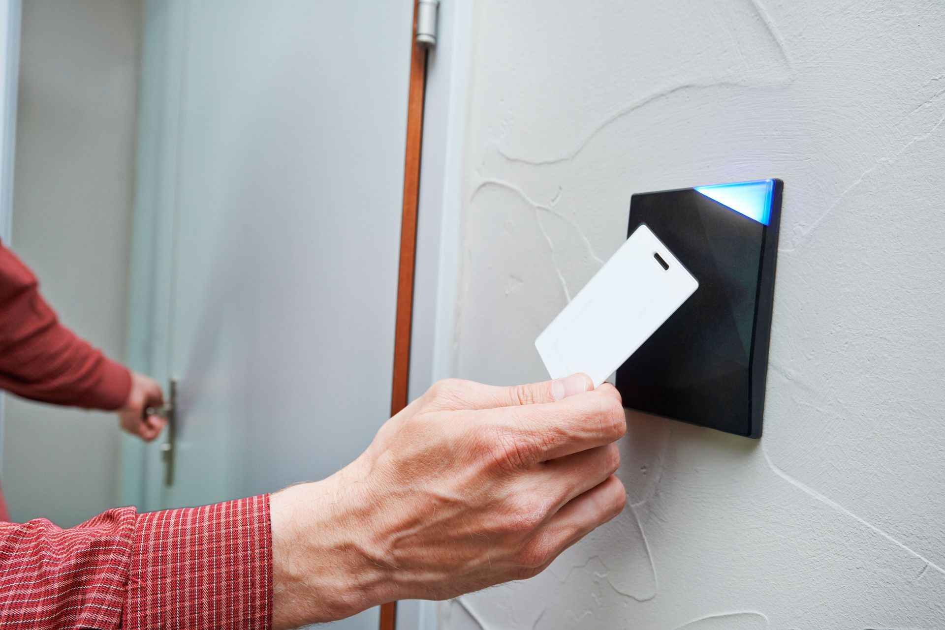 Person using access card to unlock a door with a black card reader on a textured wall.