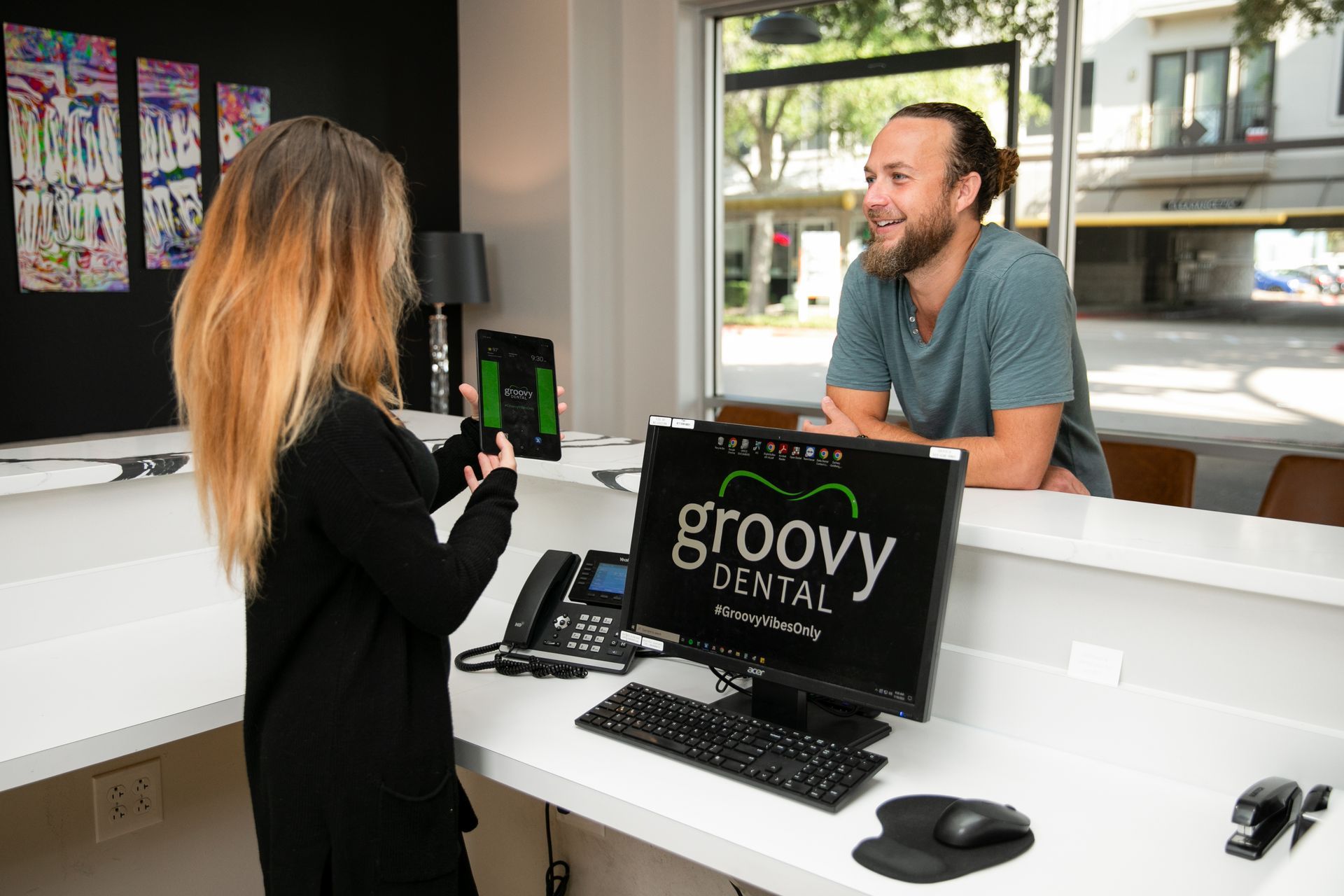 Reception desk at Groovy Dental, with a staff member helping a smiling visitor through a glass window.