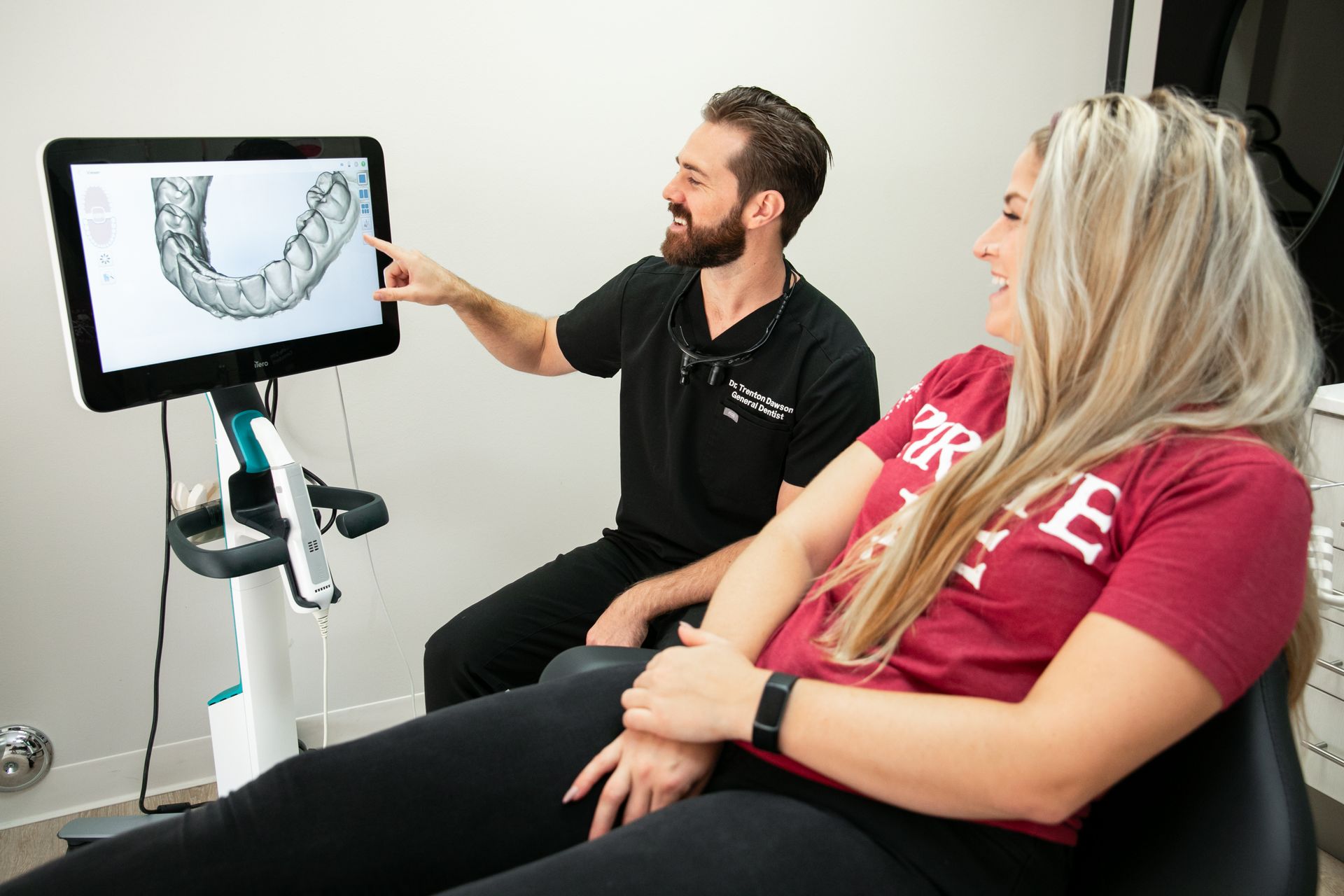 Dentist showing a 3D jaw scan on a screen to a seated patient in a clinic room