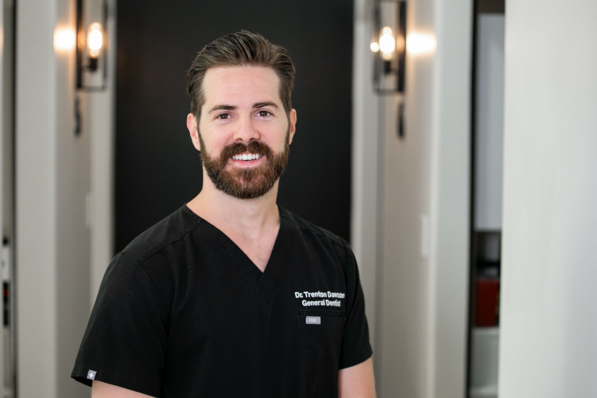 Man in black scrubs smiling in a bright hallway