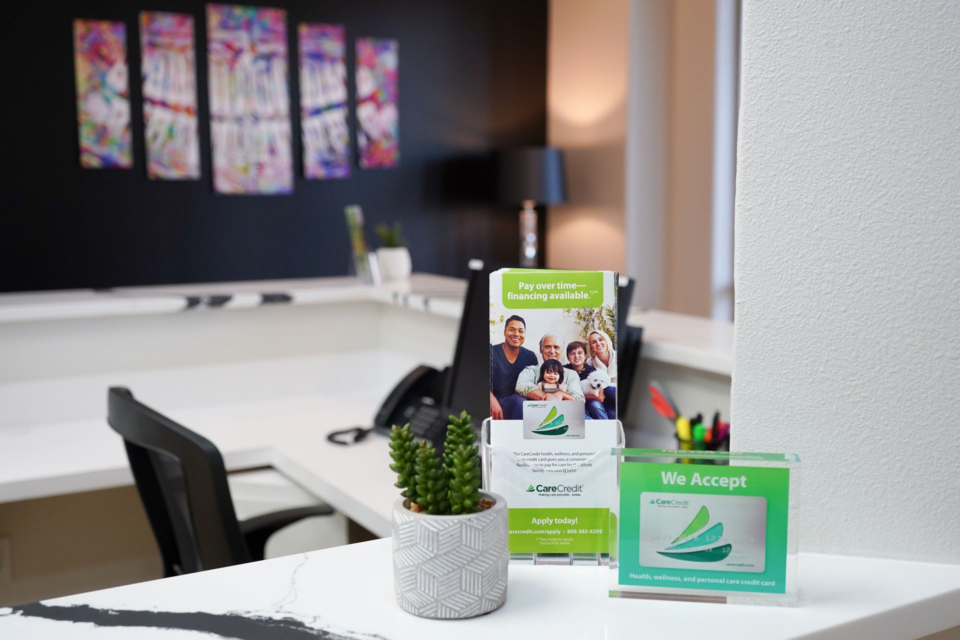 Desk display with green brochures, a potted plant, and office chairs in a modern workspace