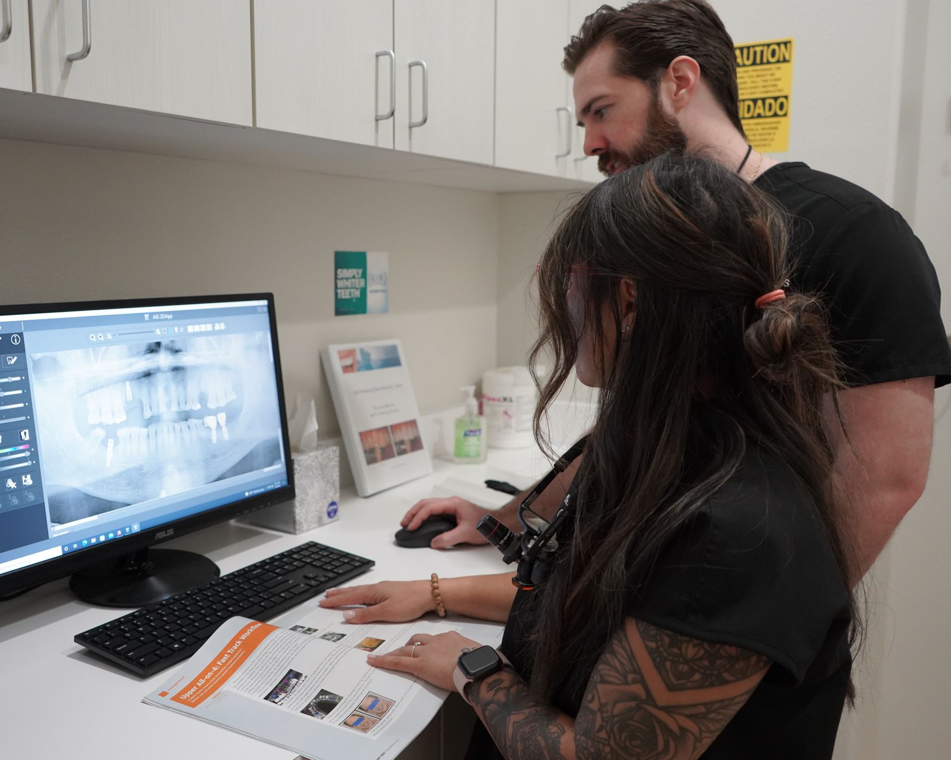 Two people reviewing dental X-rays on a computer in a clinic