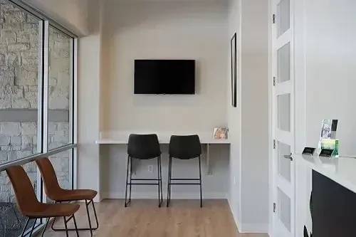 Modern waiting area with wall-mounted TV, two black stools, and a small white counter.