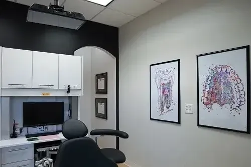 Small exam room with cabinets, computer desk, chair, and two framed anatomical spine posters on the wall.