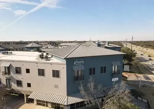 Aerial view of a blue-and-beige building in a suburban neighborhood under a clear sky