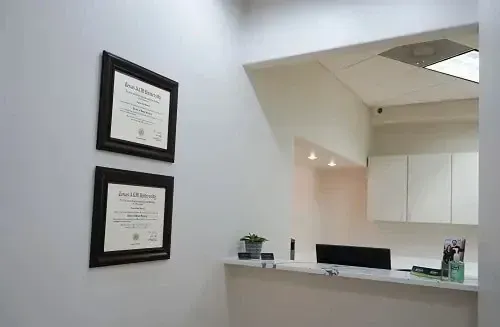 Office reception desk with two framed certificates on a white wall and a ceiling light above