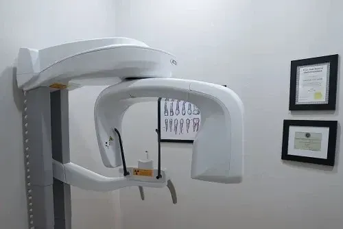 Dental X-ray machine in a clinic room with framed certificates on the wall
