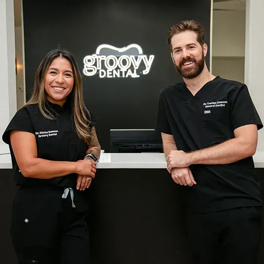 Two dental staff members in black uniforms standing at the Groovy Dental reception desk