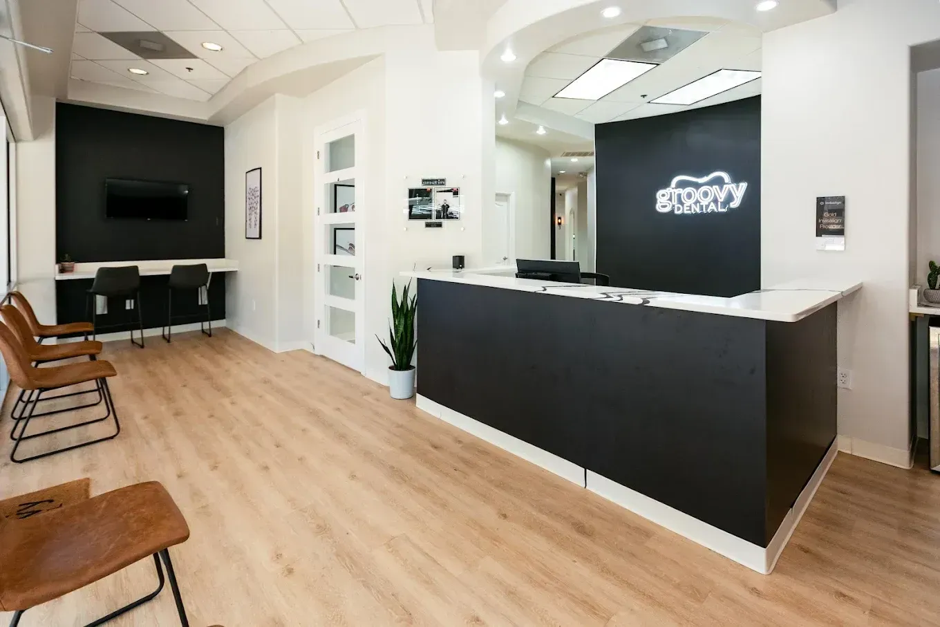 Modern reception area with black front desk, wood floors, wall-mounted TV, and seating chairs