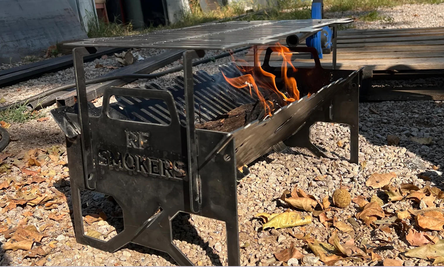 Metal smoker with flames burning inside, grill over coals. Set outdoors.