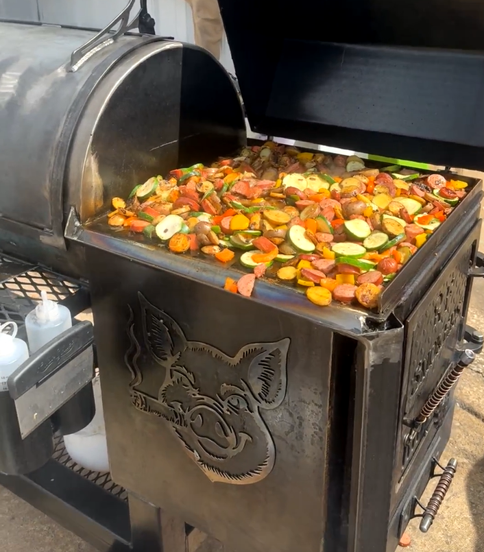 Smoker with roasted vegetables on a metal surface; outdoors.