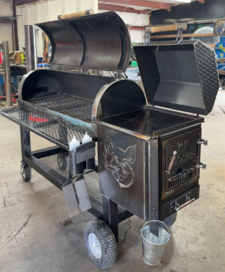 Black metal smoker with open lids, grilling area, and side firebox.