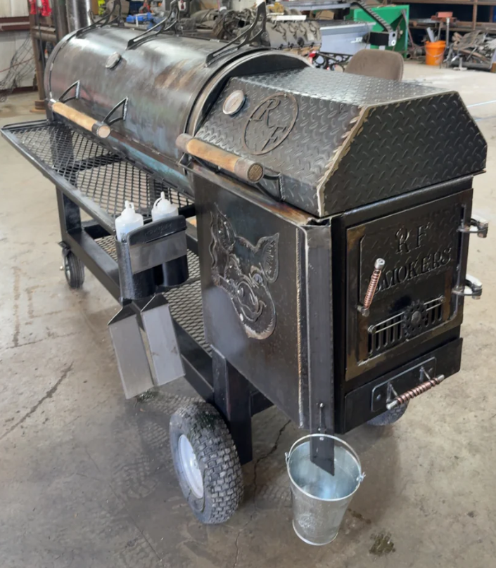 Large, custom-built smoker grill with a firebox, side shelf, and a bucket, on wheels.