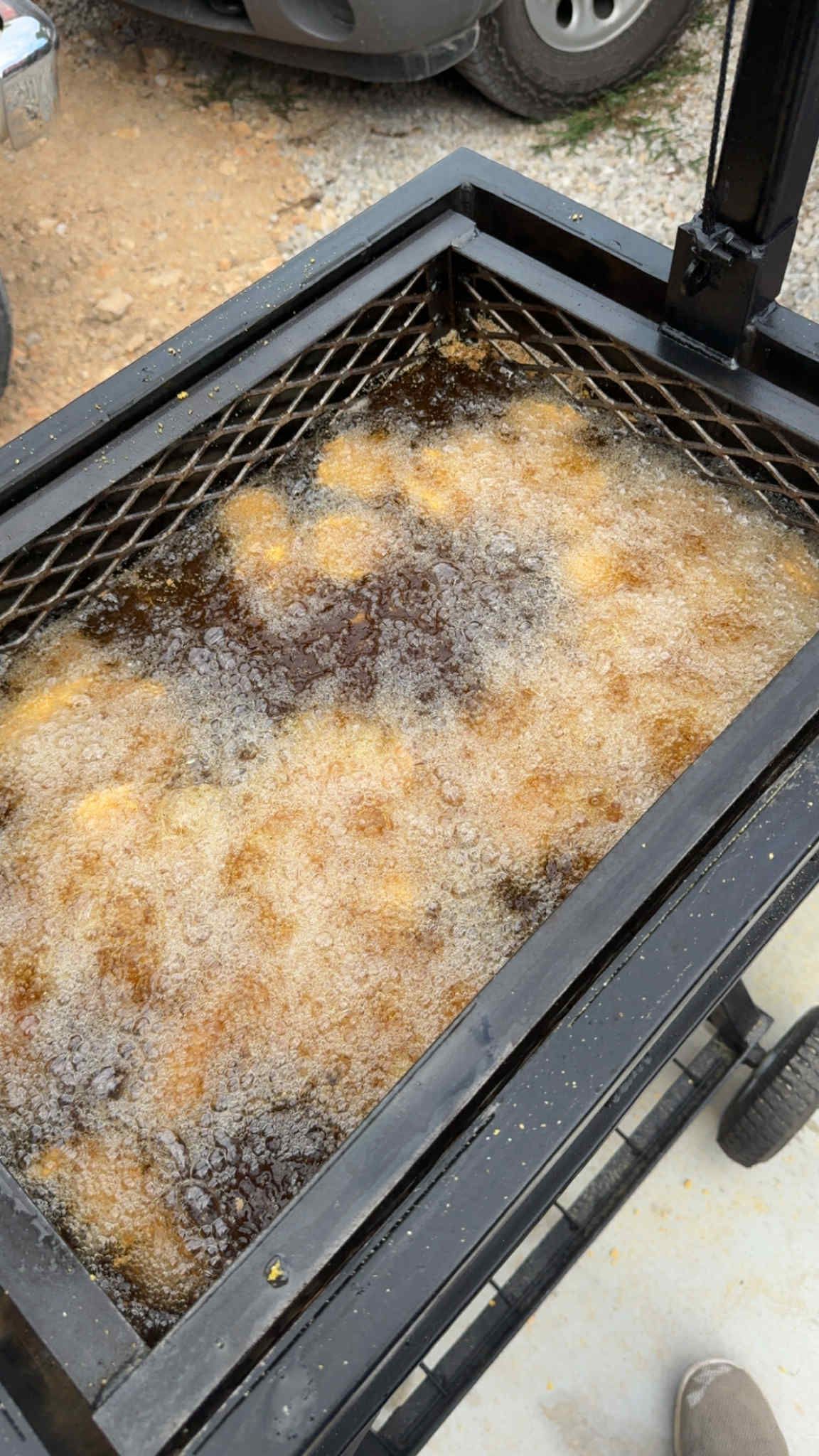 Black deep fryer with many items being fried in bubbling oil.