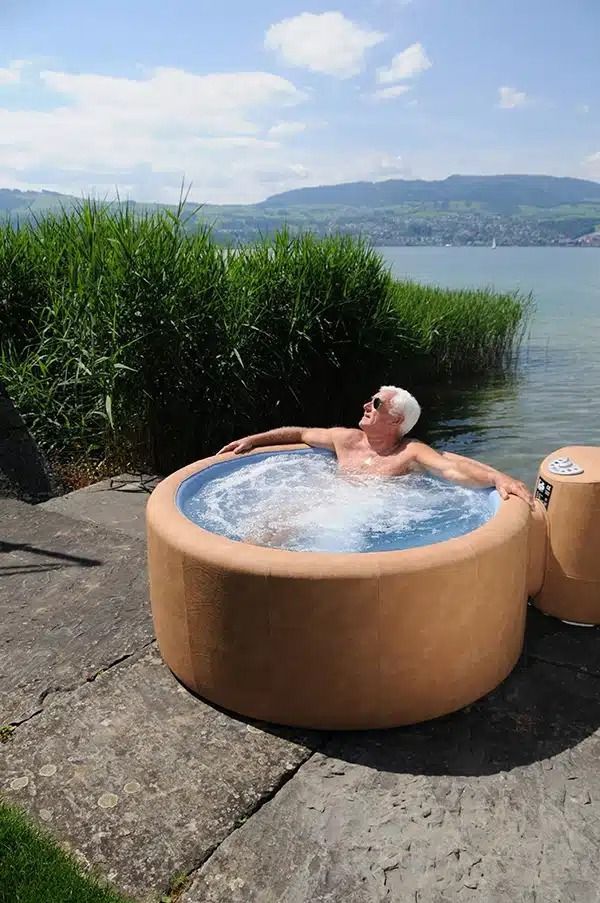 Man relaxing in a hot tub by a lake on a sunny day.