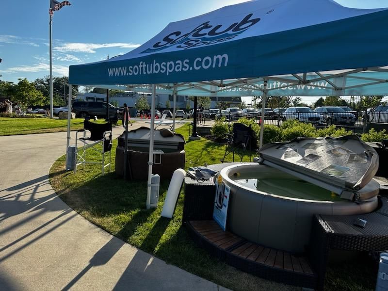Hot tubs displayed under a blue tent for sale, outdoors on a sunny day.