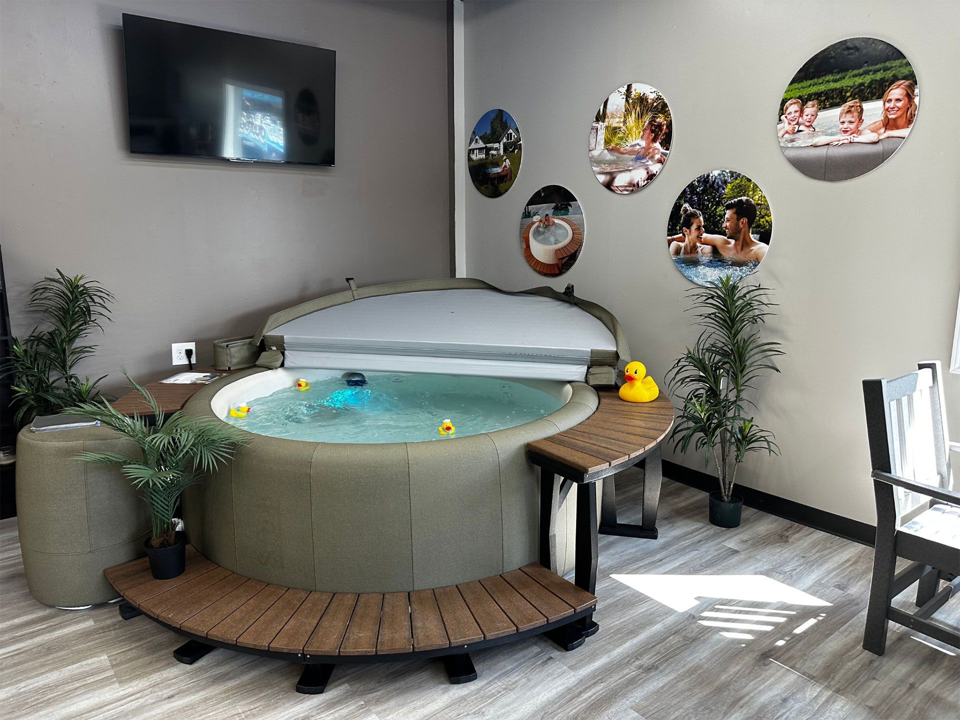 Hot tub in a room with decorative plants, a TV, and oval photos on the wall. Rubber ducks float in the water.