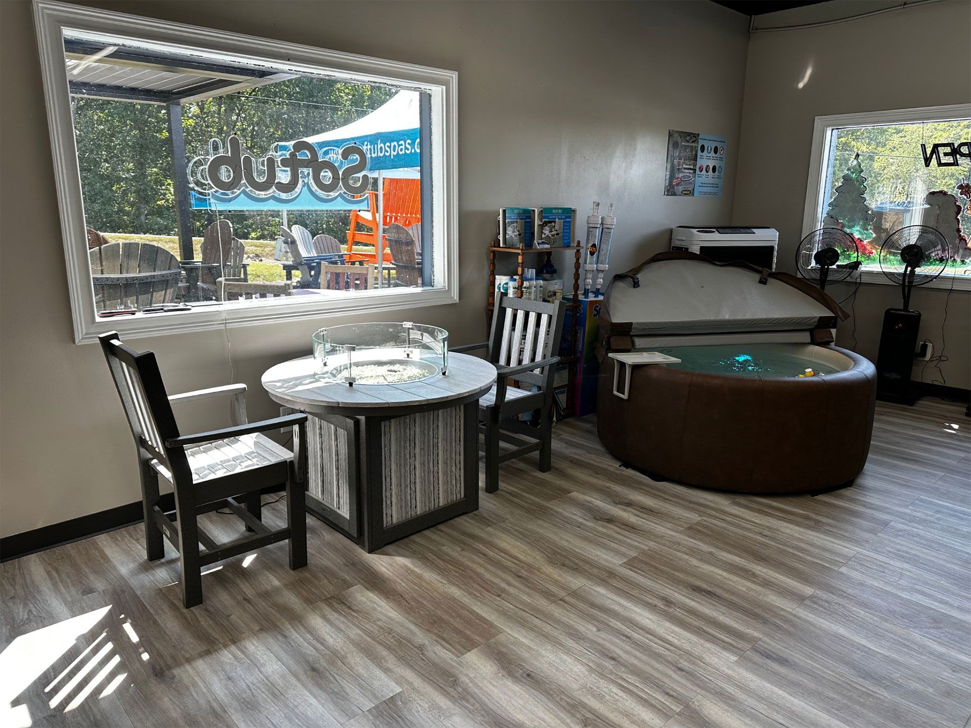 Indoor showroom with hot tub, table, chairs, and large windows.