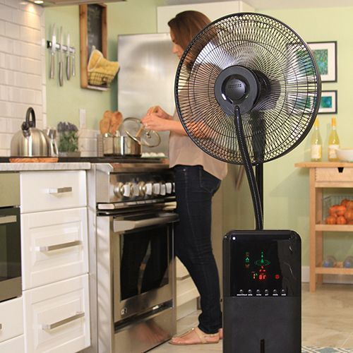 Woman cooking in kitchen, fan blowing. Black appliance, stainless steel, light wood, white cabinets.