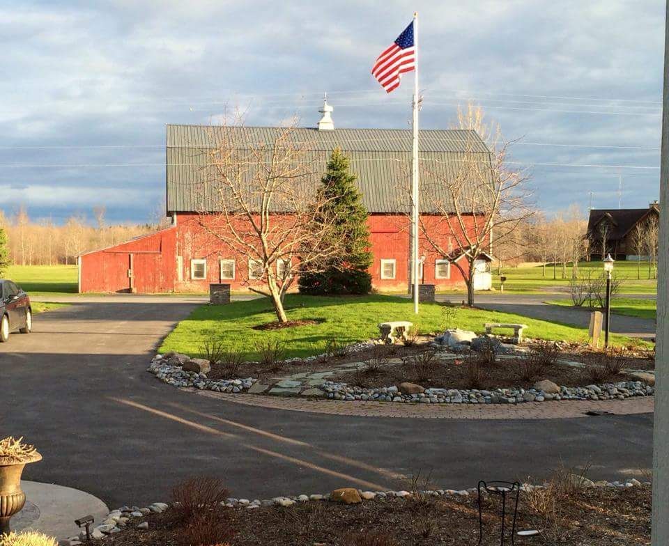 Red barn with American flag and circular driveway on a sunny day.