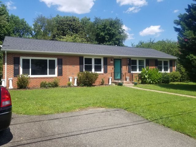 Single-story brick house with teal front door, green lawn, and driveway under a blue sky
