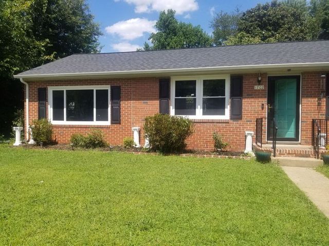 Single-story brick house with green door, white-trim windows, and a well-kept front lawn under a blue sky