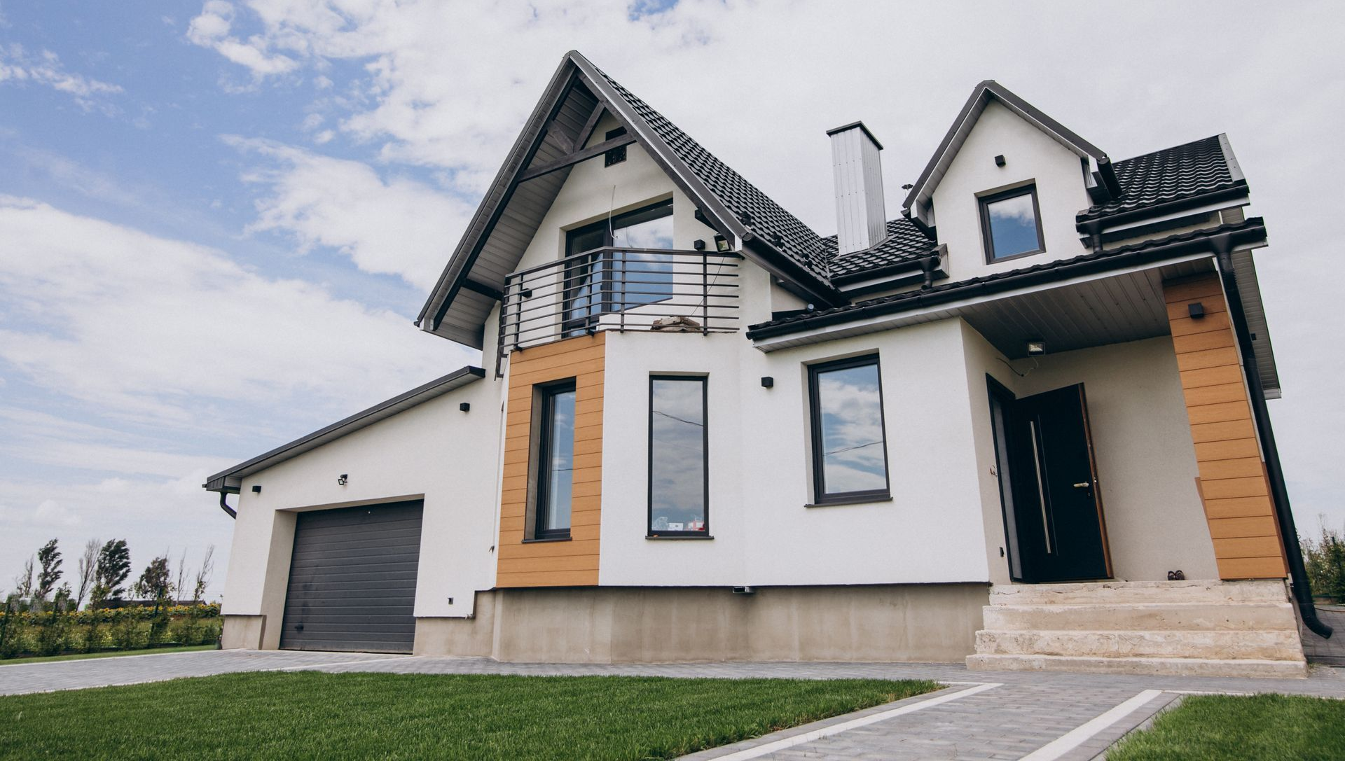Modern white two-story house with dark roof, orange accents, garage, and lawn under a cloudy sky