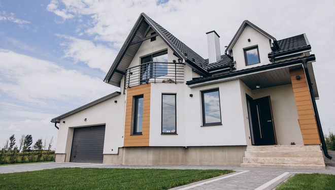 Modern white two-story house with dark roof, orange accents, garage, and lawn under a cloudy sky
