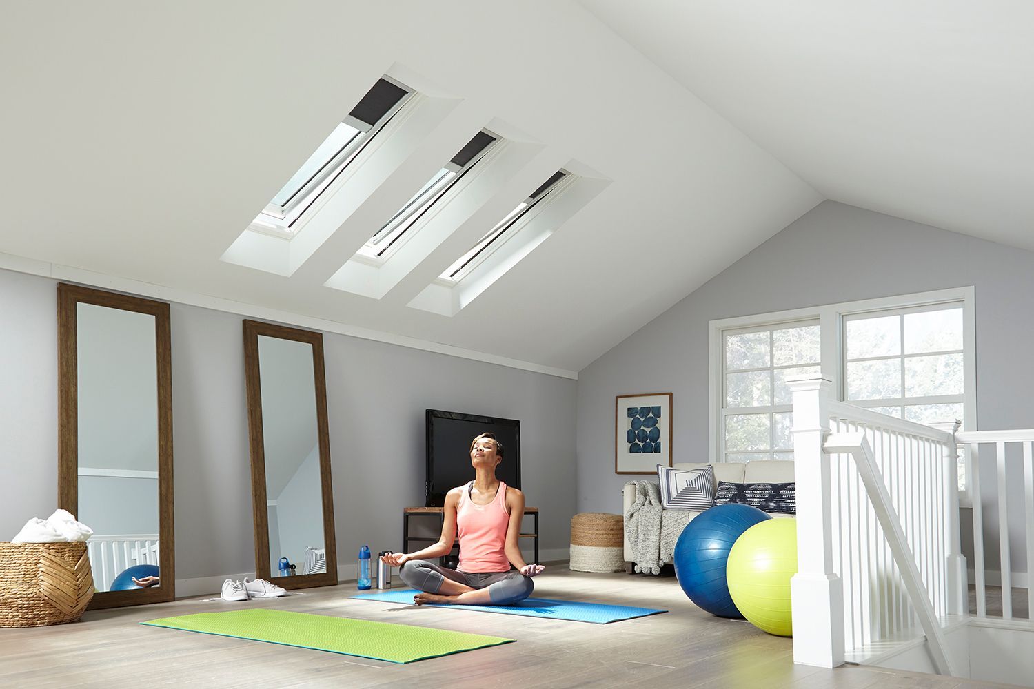 A woman is sitting in a lotus position on a yoga mat in a room.