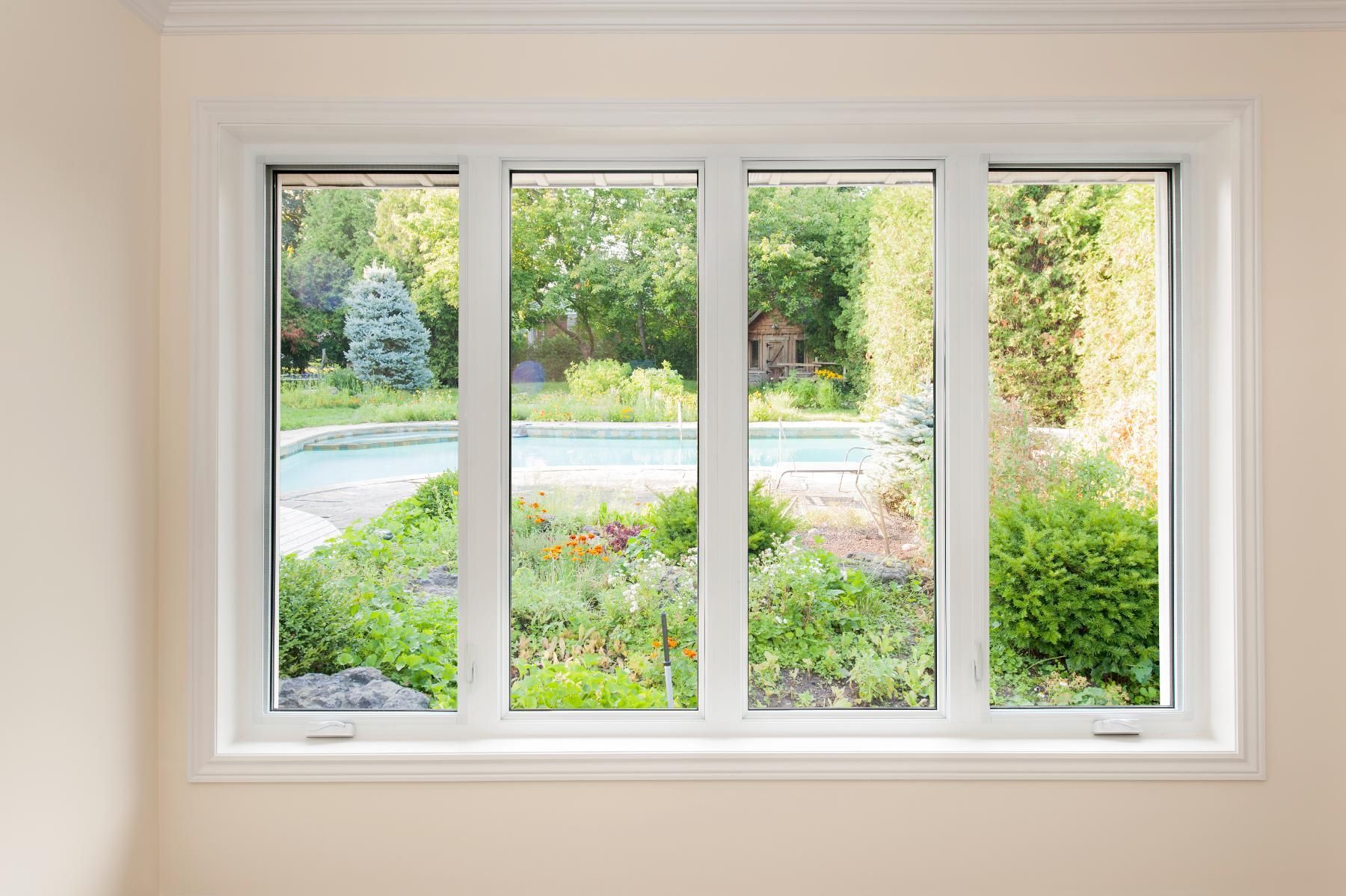 A large white window with a view of a garden and a pool.