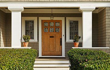 The front door of a house with a wooden door and a porch.