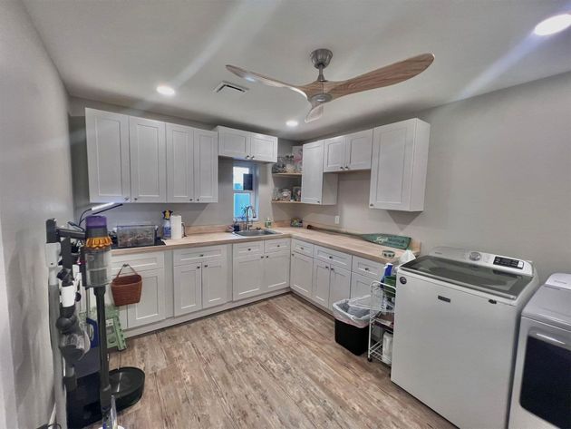 Bright kitchen with white cabinets, wood-look floor, and a ceiling fan; washer and dryer on the right.