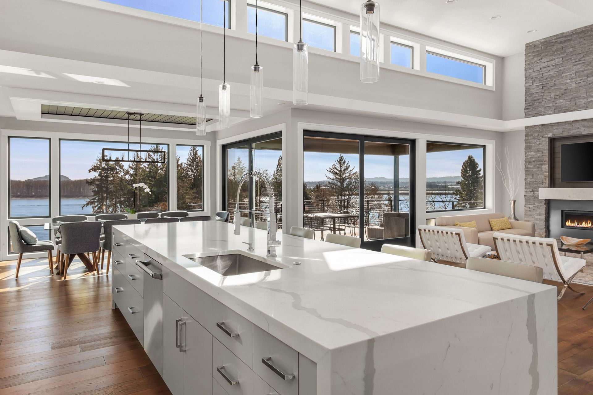 Bright modern kitchen and living room with ocean views, large windows, white island, and hardwood floors