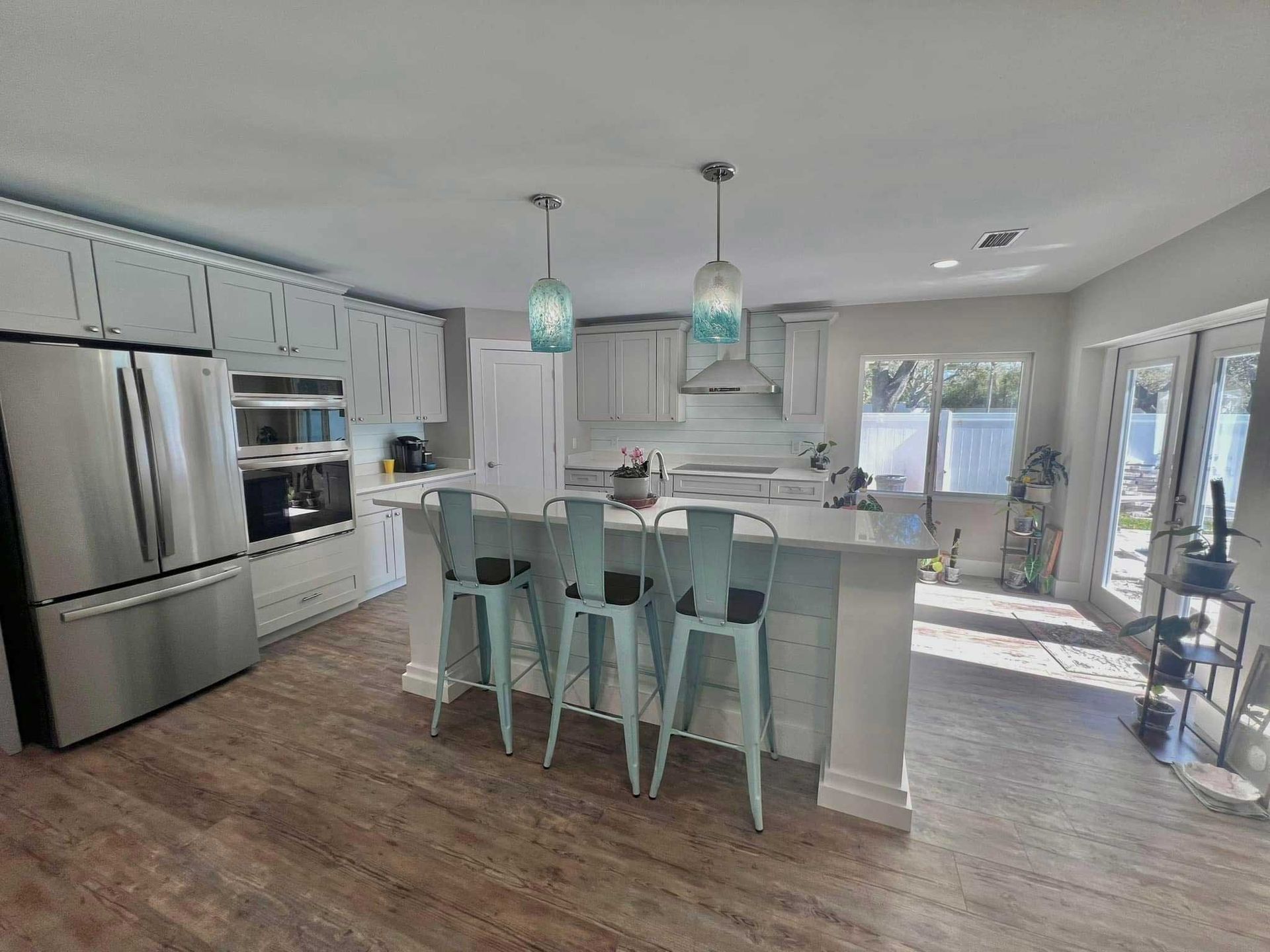 Bright modern kitchen with stainless steel appliances, island stools, and pendant lights, opening to a sunlit dining area