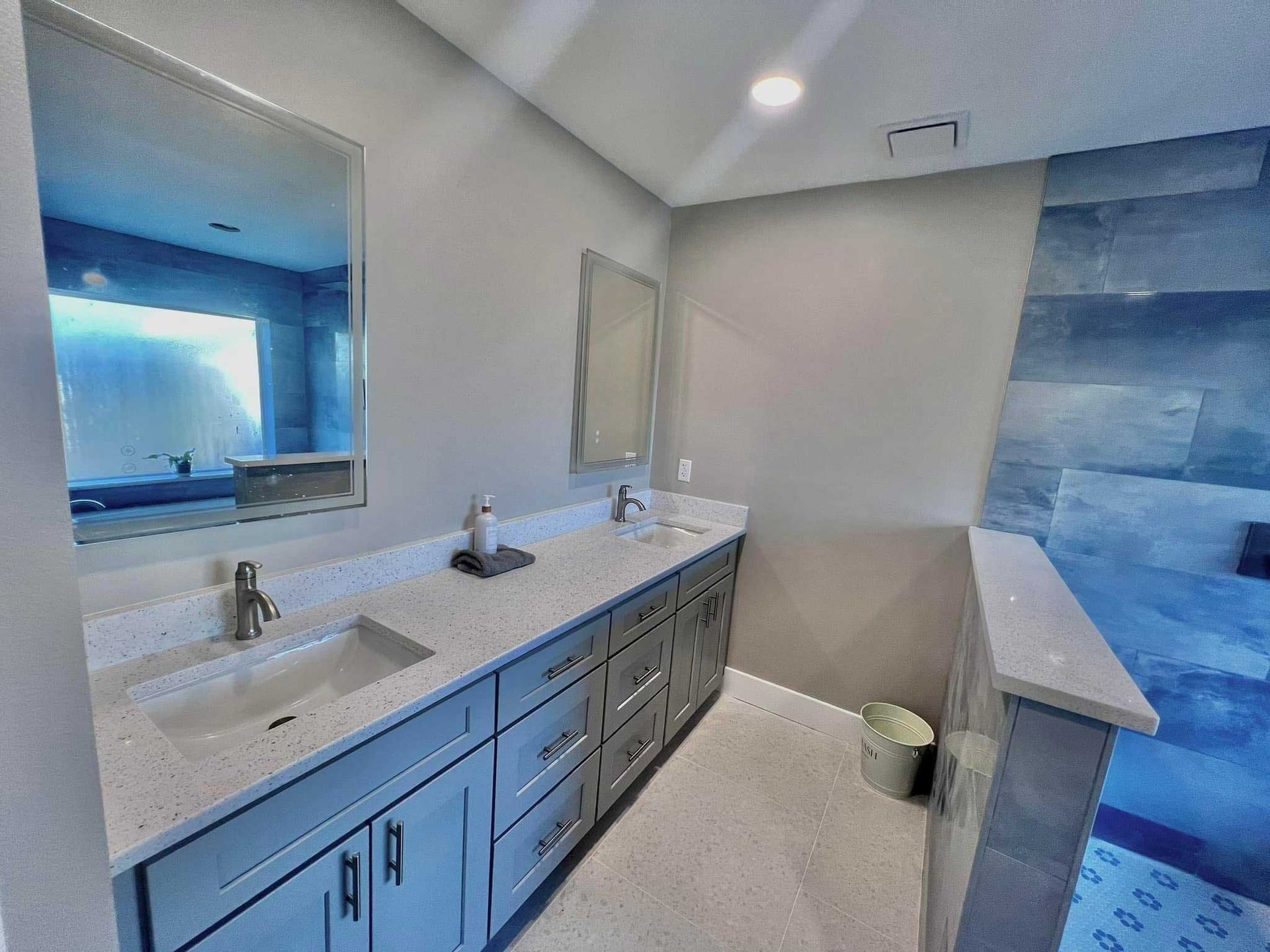 Modern bathroom with double vanity, white counters, large mirror, and blue tiled shower area